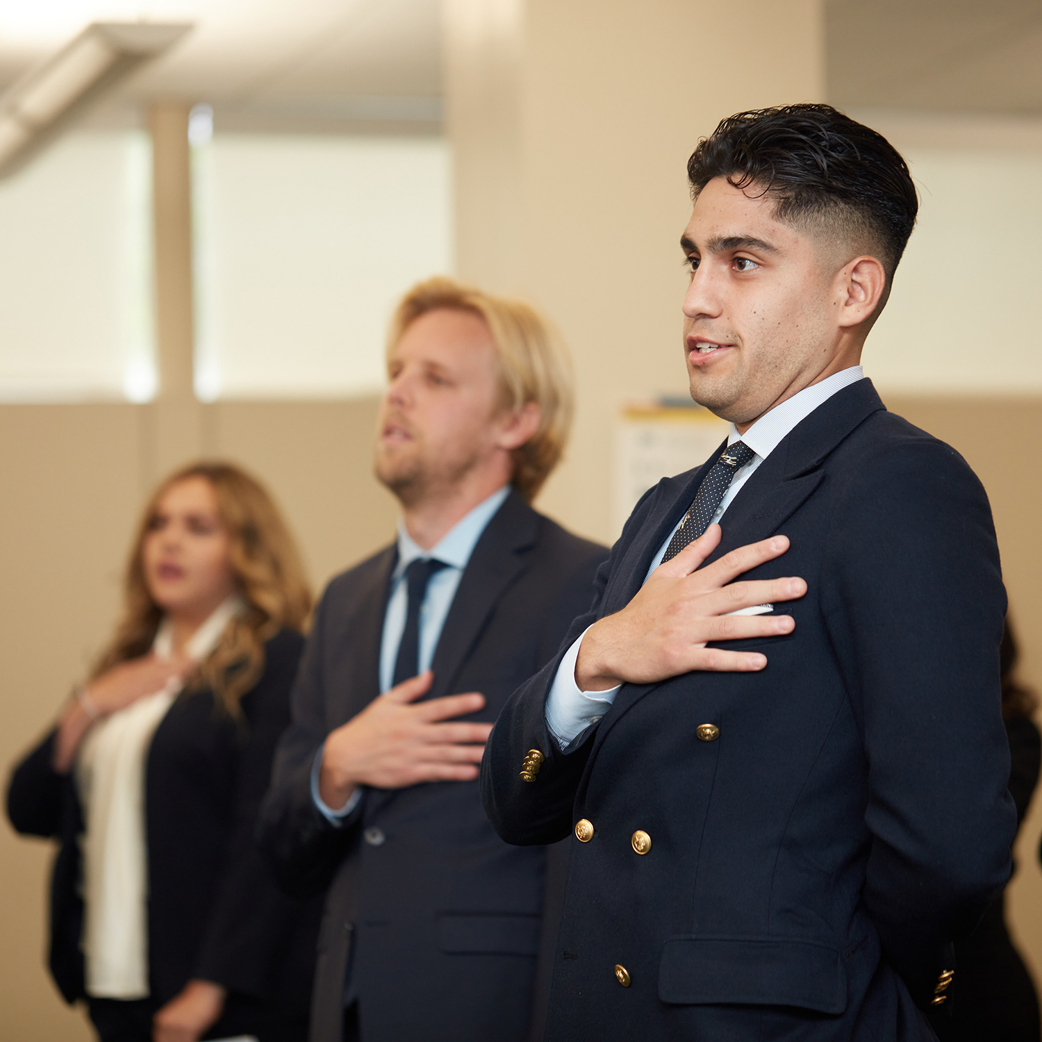 three people placing their right hand over their heart, at a swear in ceremony